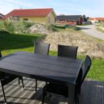 Schwarzer Tisch mit vier Stühlen auf Terrasse. Gras und Häuser im Hintergrund.