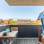 Terrace with table, chairs, and blue-white sunshade. View of houses and sky.