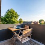 Terrace with table and two chairs, view of trees and rooftops.