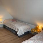 Zwei Betten mit gemusterten Bettwäschen und Nachttischen mit Lampen unter schrägen Wänden.