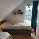 Schlafzimmer mit Dachschräge, Bett, Nachttisch und Fenster mit Blick nach draußen.