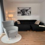 Ein Wohnzimmer mit schwarzem Sofa, grauer Sessel und Wandbild eines Hochlandrindes.