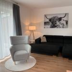 Ein Wohnzimmer mit schwarzem Sofa, grauer Sitzgelegenheit und Wandbild eines Highland-Rindes.