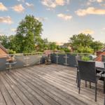 Terrasse mit Sitzgelegenheit, Tisch und Stühlen. Blick auf grüne Bäume und Wohnhäuser.