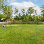 Grüner Rasen mit Kinderspielplatz und Holzzaun im Hintergrund.