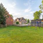 Grüner Garten mit Spielplatz und mehreren Häusern im Hintergrund.