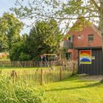 Haus mit Garten, Spielplatz und Bäumen. Eingangstür mit Schild.