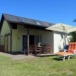 Haus mit Terrasse, Tisch, Stühlen und Liegestuhl unter Sonnenschutz.