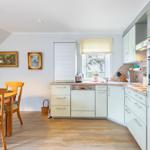 Kitchen with dining area, light cabinets, and wooden floor. Window with garden view.