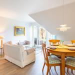 Living and dining area with wooden table, chairs, and sofa. Glass door to terrace.