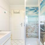 Bathroom with shower, mirror, and sink. Shower wall shows beach motif.