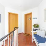 Hallway with wooden doors, red tiled floor, and white sofa with cushions.