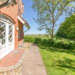 Red brick house with white doors. Path leads through meadow to a forest.