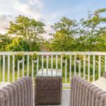 Terrace with wicker furniture and hanging planters. View of green trees and a garden.