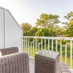 Terrace with wicker seating and flowers on white railing.