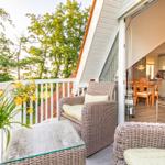 Terrace with wicker furniture and view of green trees. Kitchen area visible through glass wall.