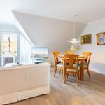 Living and dining area with wooden table, sofa, and TV. Terrace via glass doors.