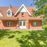 Red brick house with white window frames and dormers. Lawn and trees in the front yard.