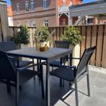 Terrace with table and chairs, surrounded by plants and wooden fence.