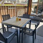 Terrace with table and chairs, wooden top, glass vases, sunlight.