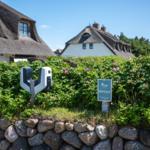 Private entrance with charging station and sign in front of traditional houses with thatched roofs.