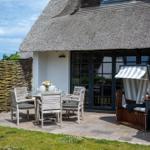 Terrace with table, chairs, and beach chair in front of a thatched house.