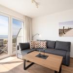 Wohnzimmer mit Sofa, Tisch und Blick auf den Strand.