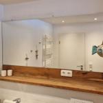 Badezimmer mit Holzwaschbecken und Spiegel. An der Wand hängt ein Fischobjekt.
