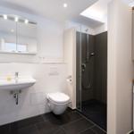 Badezimmer mit Dusche, Waschbecken und Toilette. Nebenraum mit Waschmaschine.