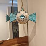 Ein hängendes Fisch-Objekt mit blauen Flossen und Augen hängt über einem Holzregal.