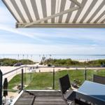 Terrasse mit Blick auf Strand und See unter einem gestreiften Markisen.