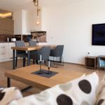 Wohn- und Essbereich mit Küchenzeile, Esstisch und Fernseher an der Wand.