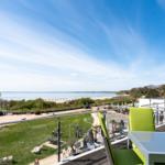 Terrasse mit grünen Stühlen und Blick auf Strand und See.