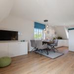 Living and dining area with TV, table and chairs, wooden floor and window with blue blinds.