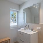Bathroom with sink, mirror, and window. Wooden stool and shower visible.