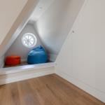 Attic room with round window, two cushions, and white cabinets.