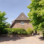 House with brick facade, slate roof, and landscaped garden. Stone wall and trees surround the entrance.