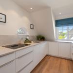 Kitchen with white cabinets, wooden floor, and large window with view of the roof