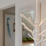White coat rack with branches, mirror in background, blue umbrella on wall.