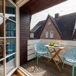 Terrace with table and two blue chairs. View of rooftops and house facades.