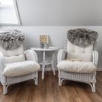 Zwei weiße Rattan-Stühle mit Fellkissen und einem Tisch dazwischen.