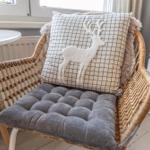 Rattan-Stuhl mit Kissen und grauer Sitzauflage vor Fenster