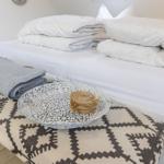 Ein Bett mit weißen Laken und Kissen. Davor steht ein Hocker mit Muster und einer Schale.