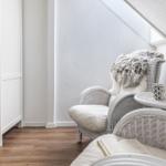 Wohnbereich mit weißen Rattan-Stühlen, kleinem Tisch und Holzboden unter Dachschräge.