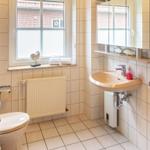 Badezimmer mit Waschbecken, Toilette und Fenster mit Blick auf Hausfassade.