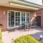 Terrasse mit Sitzgruppe, Grill und Glas-Tür zum Haus. Gelb-weiße Markise.
