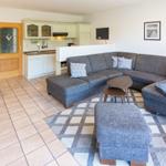 Wohnzimmer mit grauem Sofa, Teppich und Küchenbereich im Hintergrund.