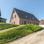 Modernes Backsteinhaus mit schwarzem Dach und grüner Umgebung.