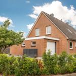 Ein zweistöckiges Haus mit rotem Backstein, Dach mit Schiebedach und Garten mit Sträuchern.