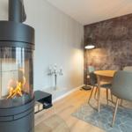 Kaminofen mit brennendem Feuer, Esstisch mit Stühlen und Wand mit Muster.